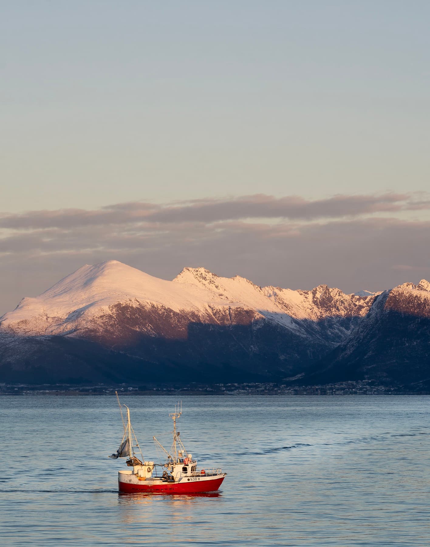 Fishing vessel below snow-capped mountains on the Norwegian coast