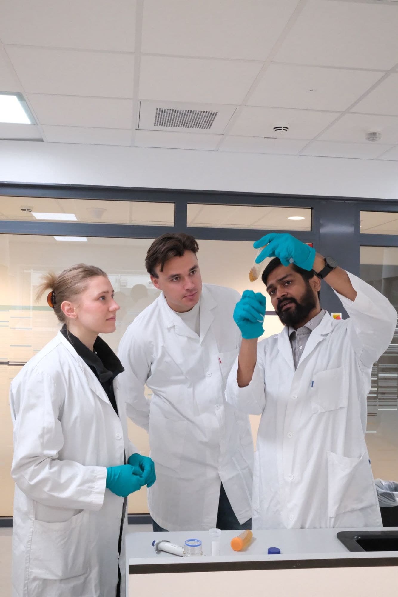 Three researchers in lab coats examining a sample tube in the laboratory